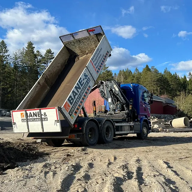 Lastebil tipper masser på anleggsplass omgitt av skog