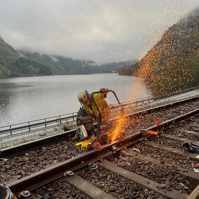 Kapping av jernbaneskinne med gnister ved innsjø og fjell