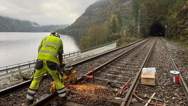 Arbeider vedlikeholder spor nær tunnel og innsjø