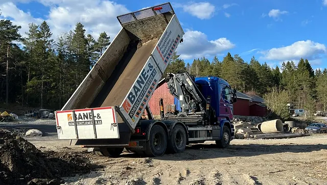Lastebil tipper masser på anleggsplass omgitt av skog
