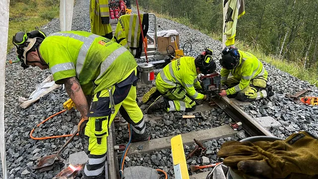 Team monterer jernbaneskinner og fester komponenter i grus