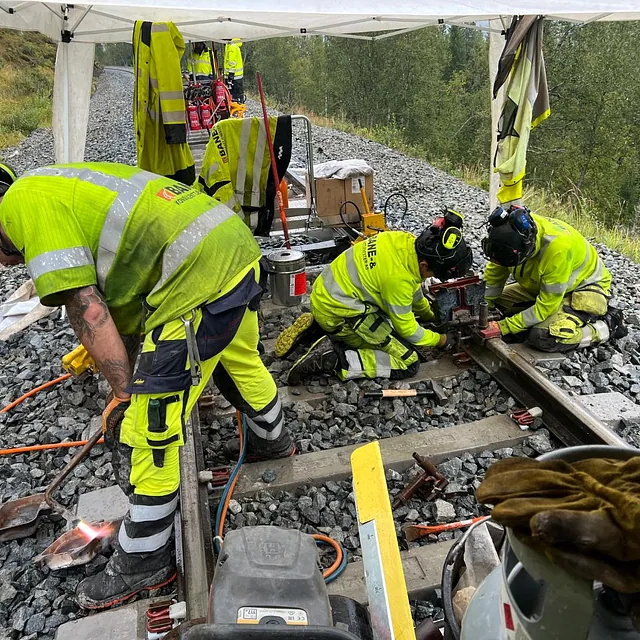 Team monterer jernbaneskinner og fester komponenter i grus