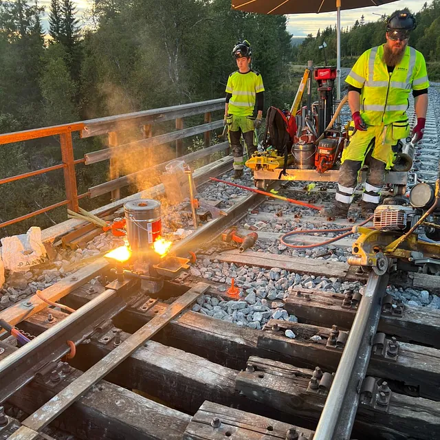 Arbeidere utfører sporarbeid med varmeutstyr på bru i solnedgang
