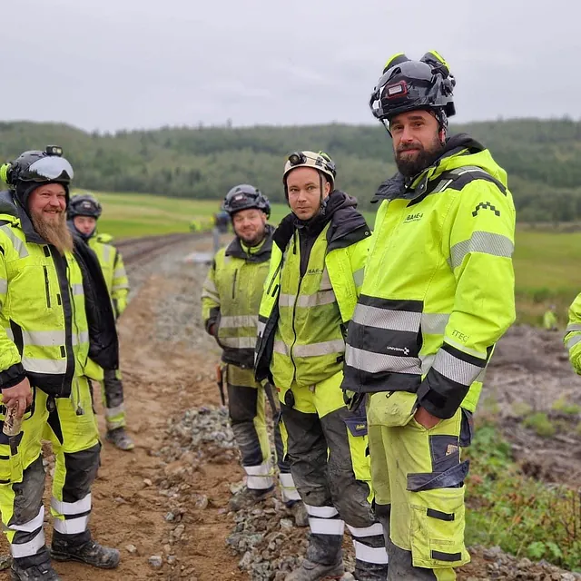 Arbeidere i høy synlighetstøy ved jernbanespor i landlig område