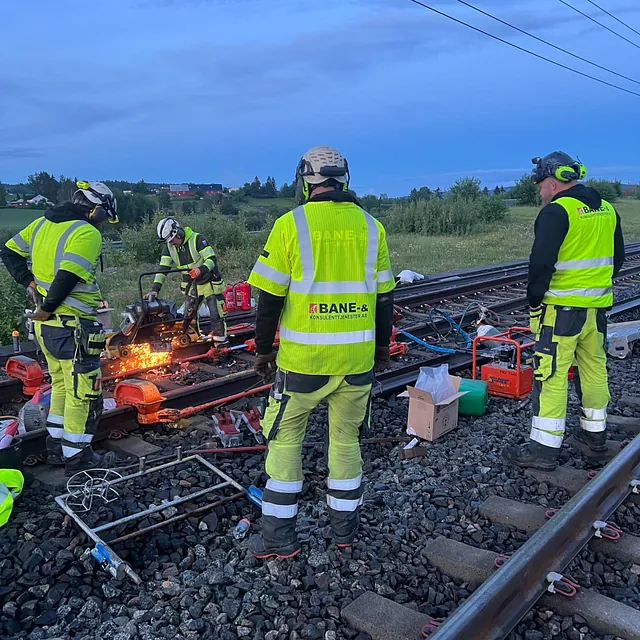 Arbeidere sveiser skinner med gnister på jernbanespor i skumring